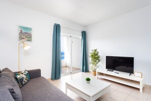 A modern living room with a sofa, a coffee table, a TV, and a sliding glass door leading to a balcony.