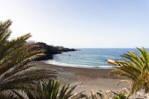 A coastal beach with rocky cliffs and a clear view of the ocean.