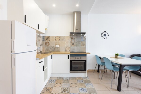 A modern kitchen with white cabinets, a built-in oven, and a stove. There is a dining area with a table and chairs.