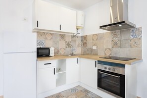 Cocina compacta con armarios blancos, microondas integrado, estufa y campana extractora.