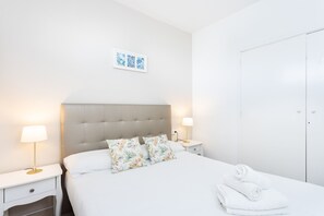 A neatly arranged hotel room with a bed, two bedside tables, a nightstand, a wall-mounted lamp, and a door. - Preciosas vistas, playa 200m, WIFI (Callao Salvaje)