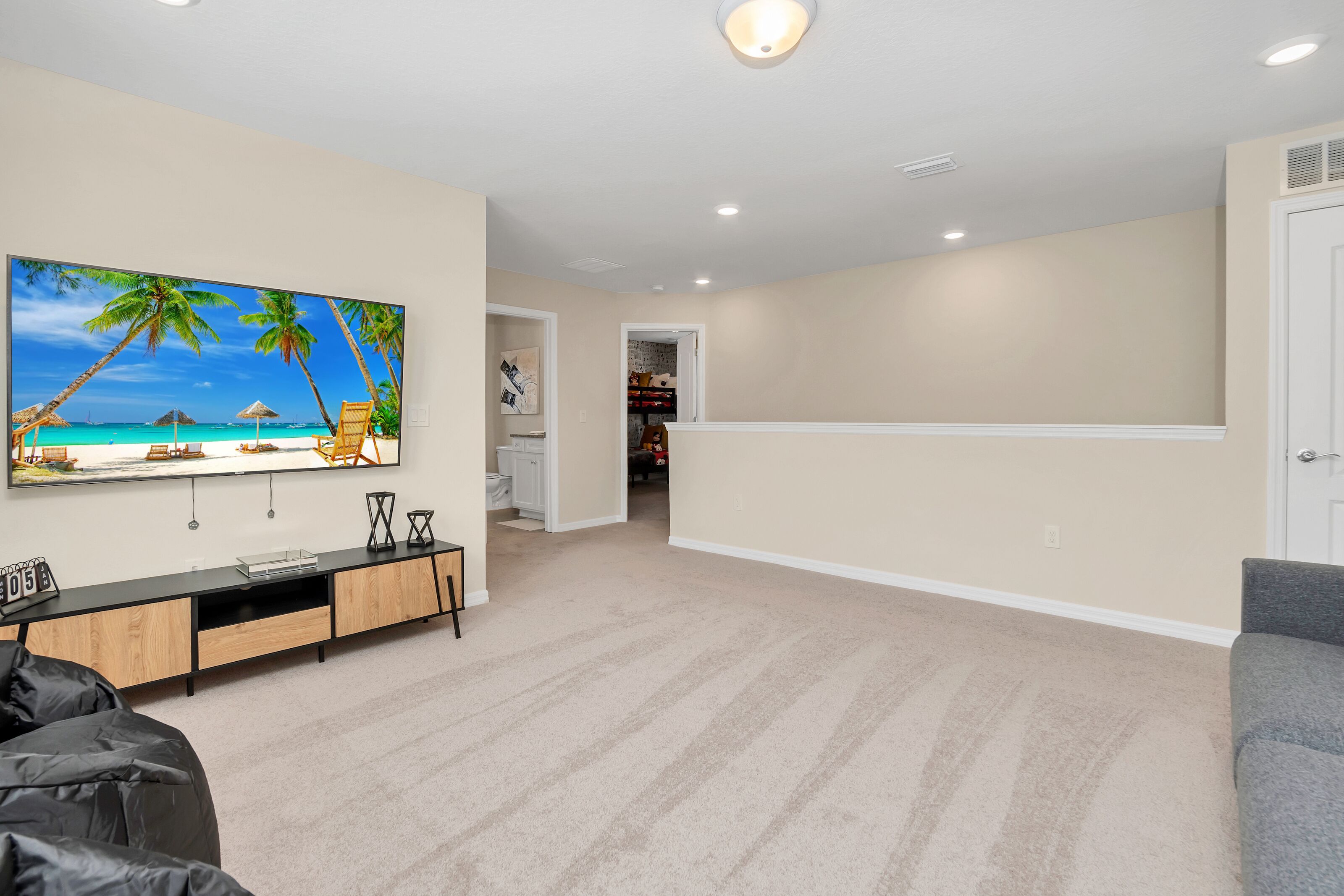 A spacious living area with a large flat-screen TV mounted on the wall, a wooden entertainment unit, and a grey sofa.