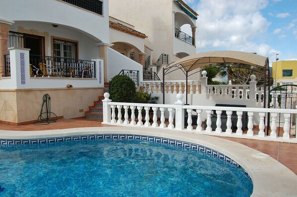 A swimming pool with a white balustrade, a covered patio, and a two-story building with balconies. - 4 Bed Fantastic Apt, Private Pool Close to Golf, Beach and Entertainment (Orihuela Costa)