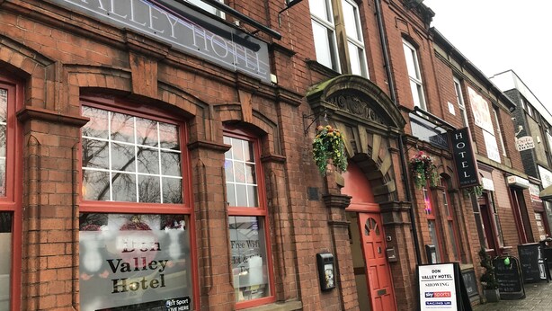 A brick building with a sign for the Valley Hotel, featuring a large window with a view of the street, a red door, and a signboard advertising a sports event. - Don Valley Hotel (Sheffield)