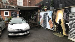 A car parked in a narrow alleyway with a mural on the wall depicting a cityscape and a bottle of beer. - Don Valley Hotel (Sheffield)