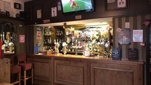 A bar area with a television displaying a sports event, shelves stocked with various liquor bottles, and a sign indicating 'No Service' and 'Free Drinks'. - Don Valley Hotel (Sheffield)