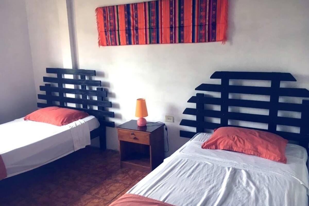 Una habitación con dos camas, cada una con cabecero de madera, una mesita de noche pequeña y una lámpara.