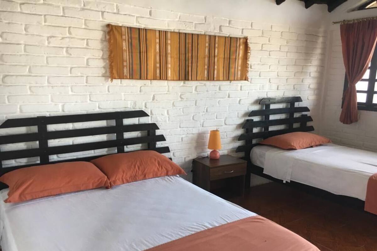 Una habitación con dos camas, ropa de cama blanca, cabeceros de madera, un tapiz a rayas y una ventana con cortinas.