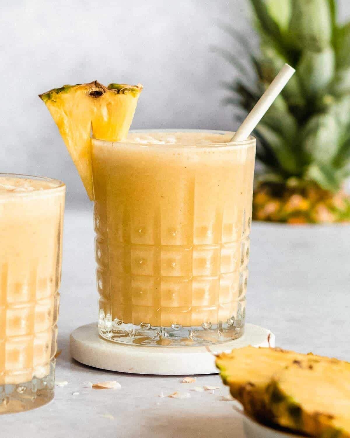 Un vaso de batido de piña con pajita y una rodaja de piña como decoración.