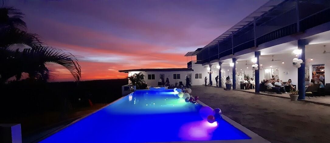 Una piscina con vistas a la puesta de sol, un área de estar cubierta al aire libre y un edificio con varias habitaciones.