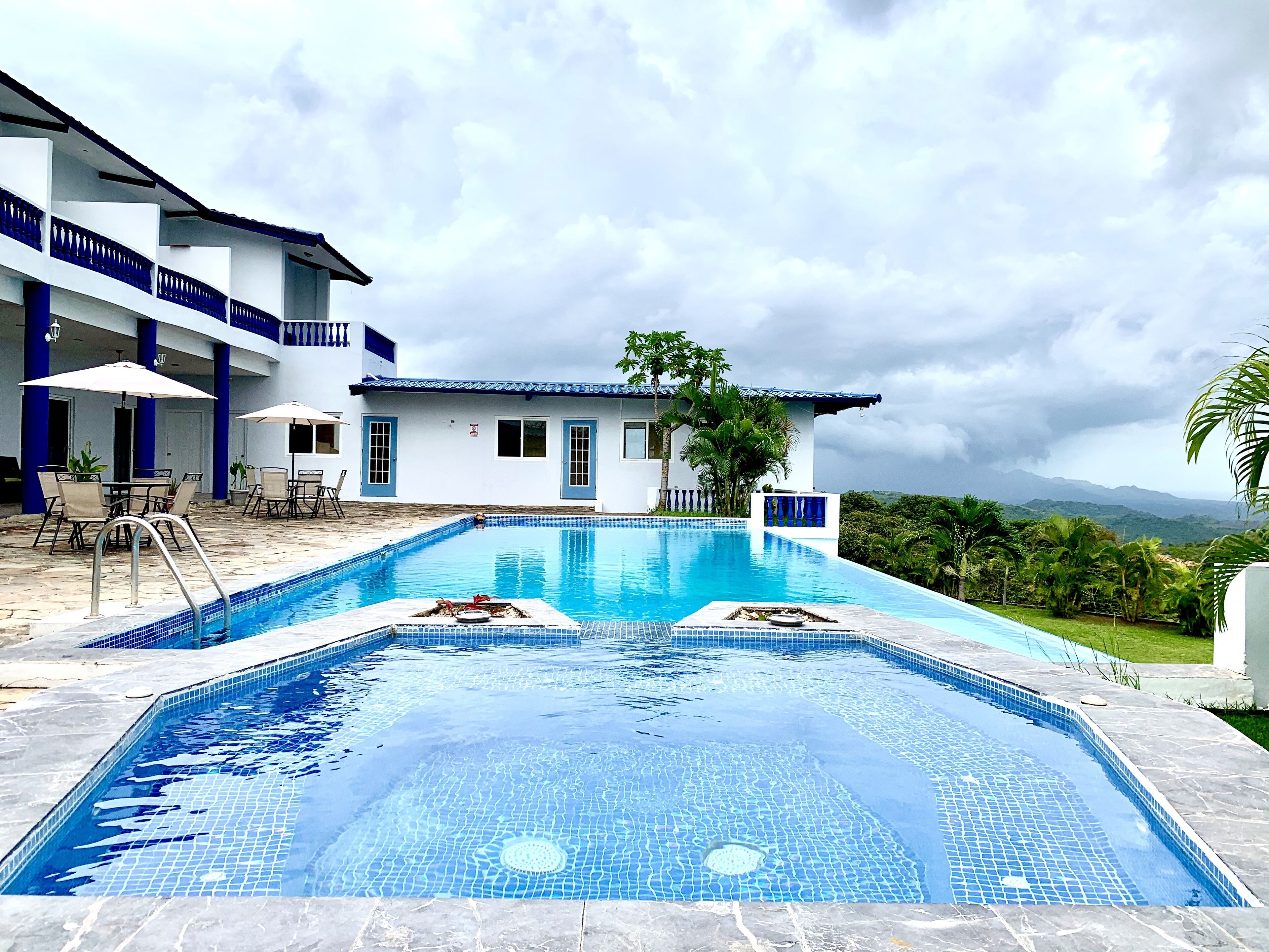 Une piscine avec une terrasse carrelée, un espace salon couvert et une vue sur une chaîne de montagnes.