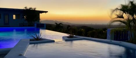 Piscina con vistas a un atardecer y montañas distantes.