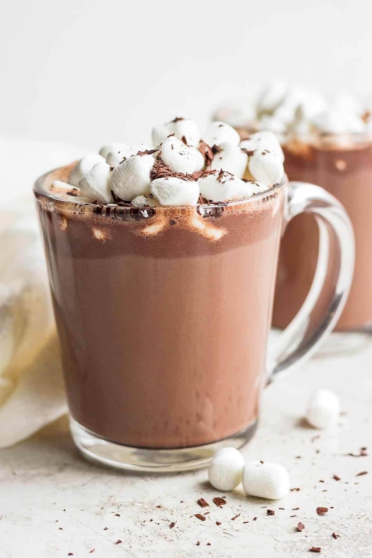 A glass mug filled with hot chocolate topped with marshmallows and chocolate shavings.