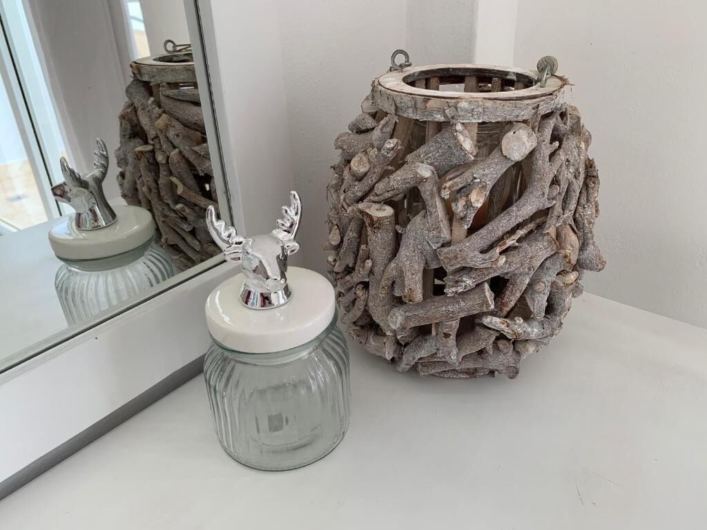 Un adorno rústico con un frasco de vidrio y una escultura de metal, sobre una superficie blanca junto a un espejo.