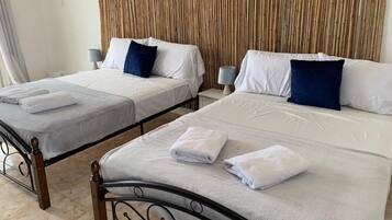 Two single beds with white linens and blue pillows, a bamboo wall, and a bedside table with a lamp.
