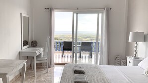 Habitación de hotel con cama, escritorio, silla, balcón con vistas y lámpara.