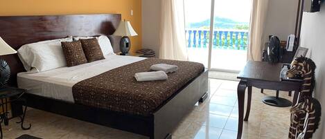 A hotel room with a large bed, a desk, and a view of the outdoors.