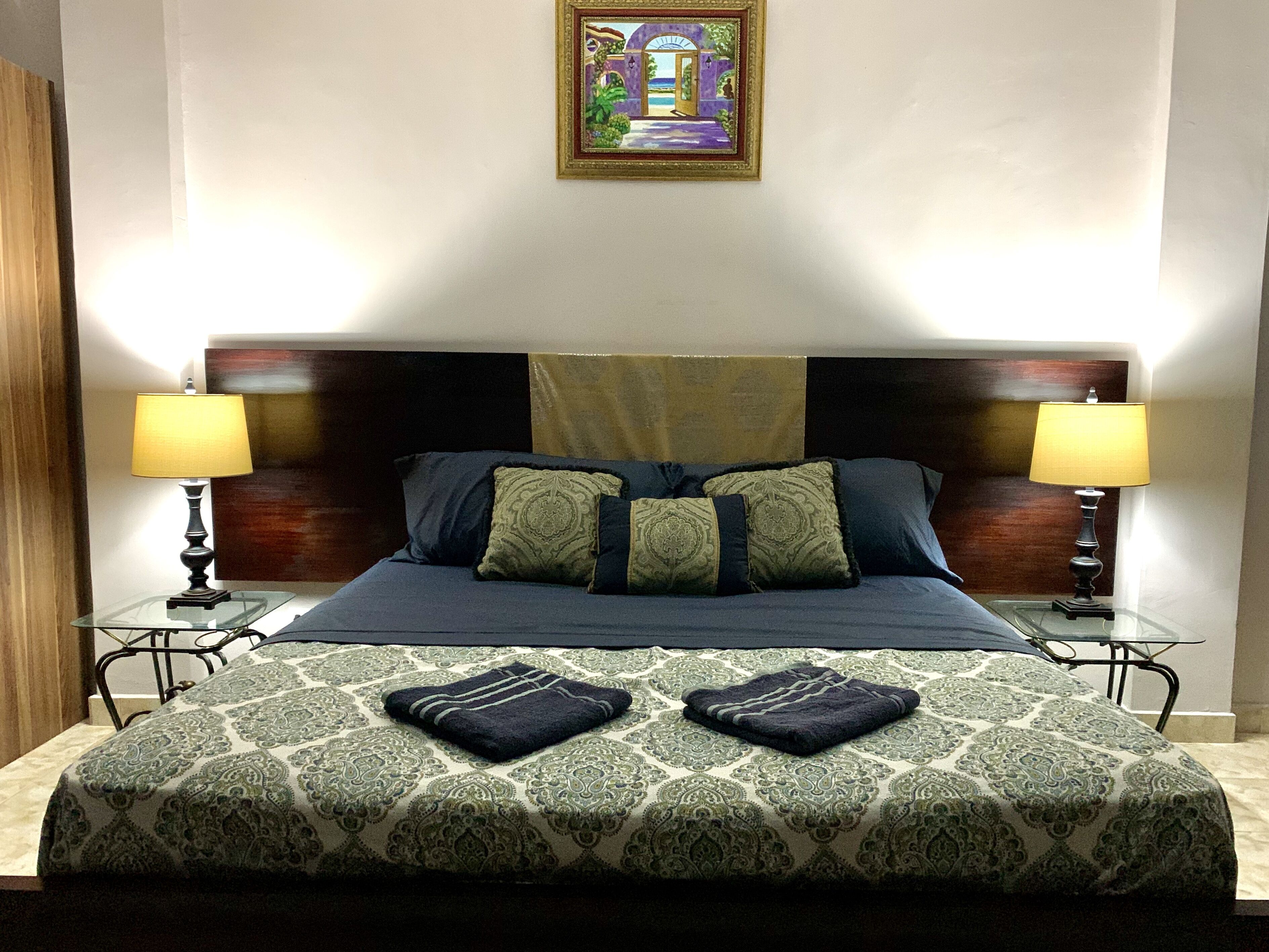 A neatly made bed with a patterned bedspread, two pillows, and two bedside lamps.