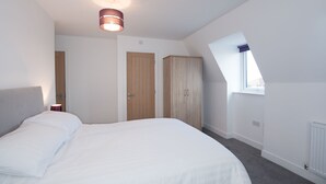 A bedroom with a large bed, a ceiling light, a wardrobe, and a window.