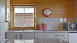 A kitchen with a window, a sink, a red kettle, a microwave, and a clock on the wall. - Baytree Lodge - UK13322 (Melbourne, near Derby)
