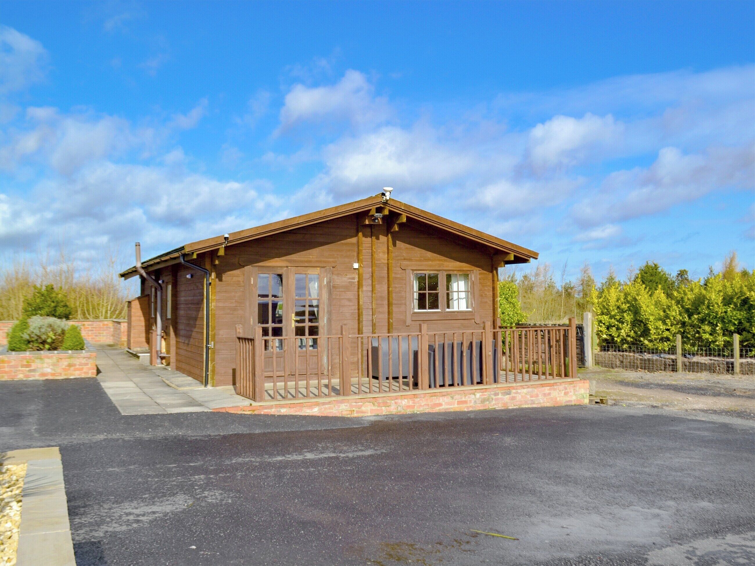 A wooden cabin with a fenced porch, a brick foundation, and a clear sky.