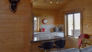 A wooden cabin interior with a kitchen area, a mounted deer head, a clock, and a window. - Baytree Lodge - UK13322 (Melbourne, near Derby)