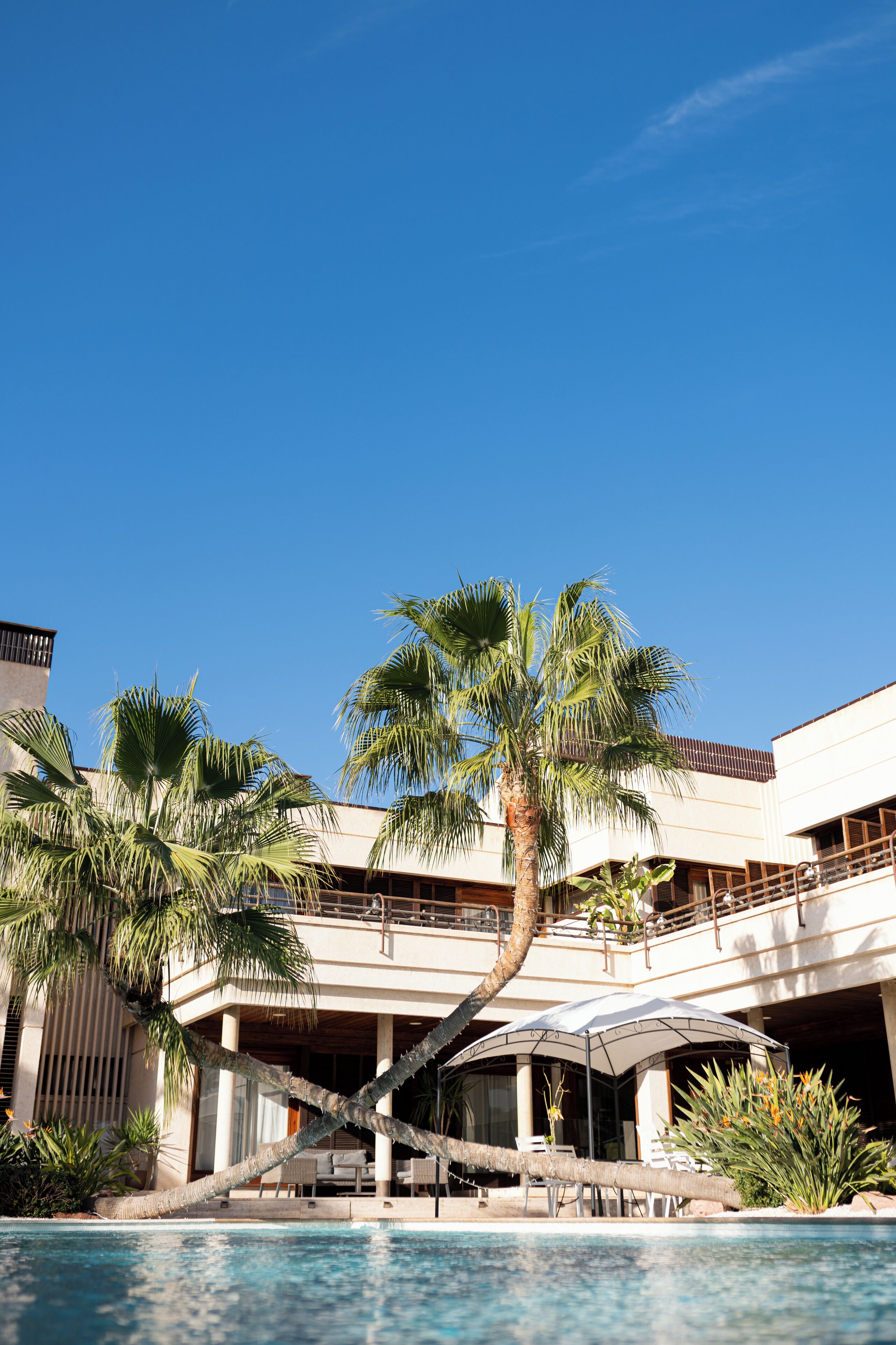 Un resort con piscina, palmeras y un edificio de dos pisos con balcones.