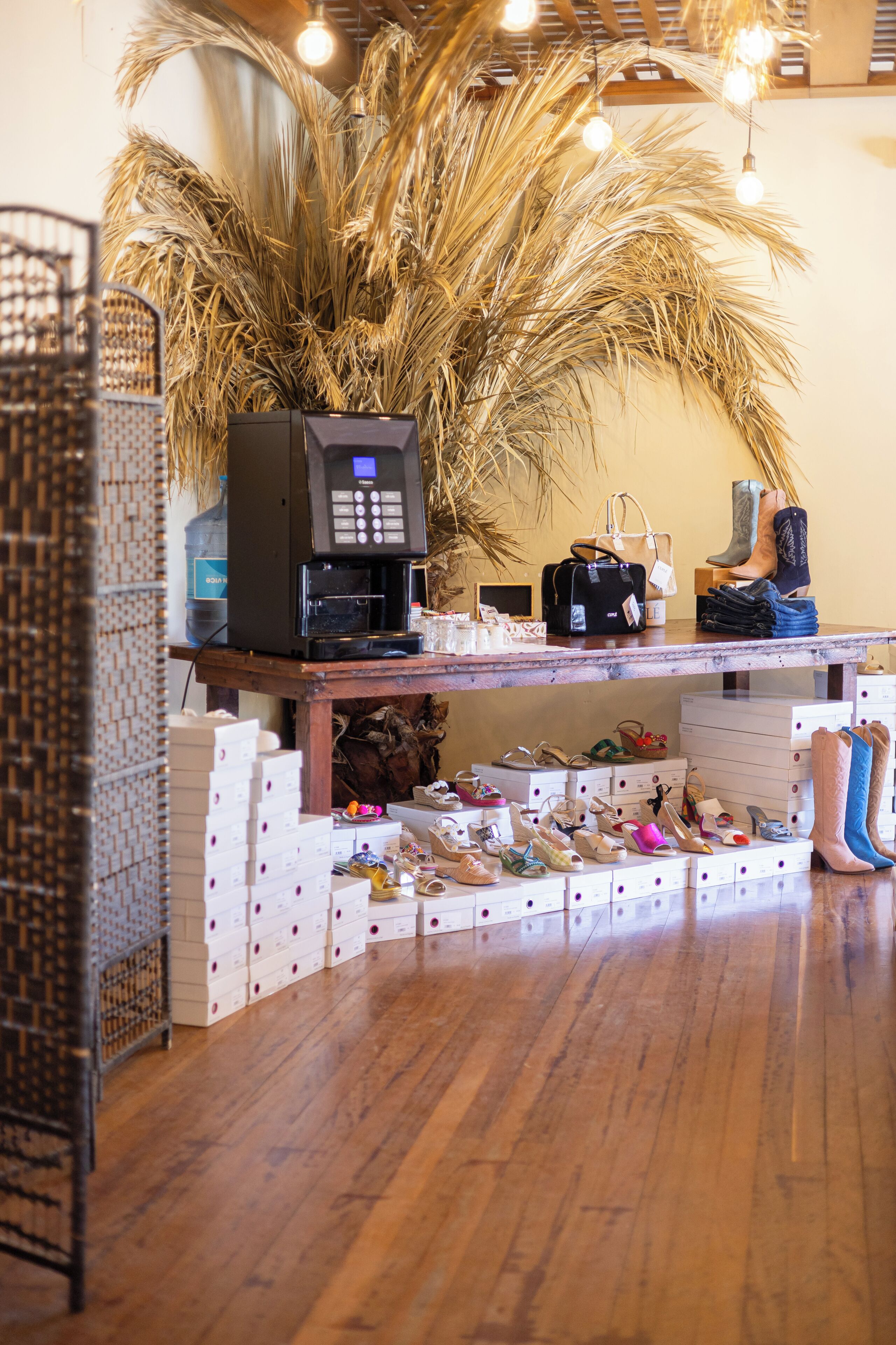 Een winkel voor schoenen met een houten vloer, een koffieapparaat en een grote sierplant.