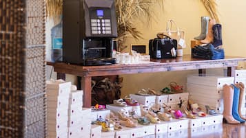 Een winkel voor schoenen met een houten vloer, een koffieapparaat en een grote sierplant.