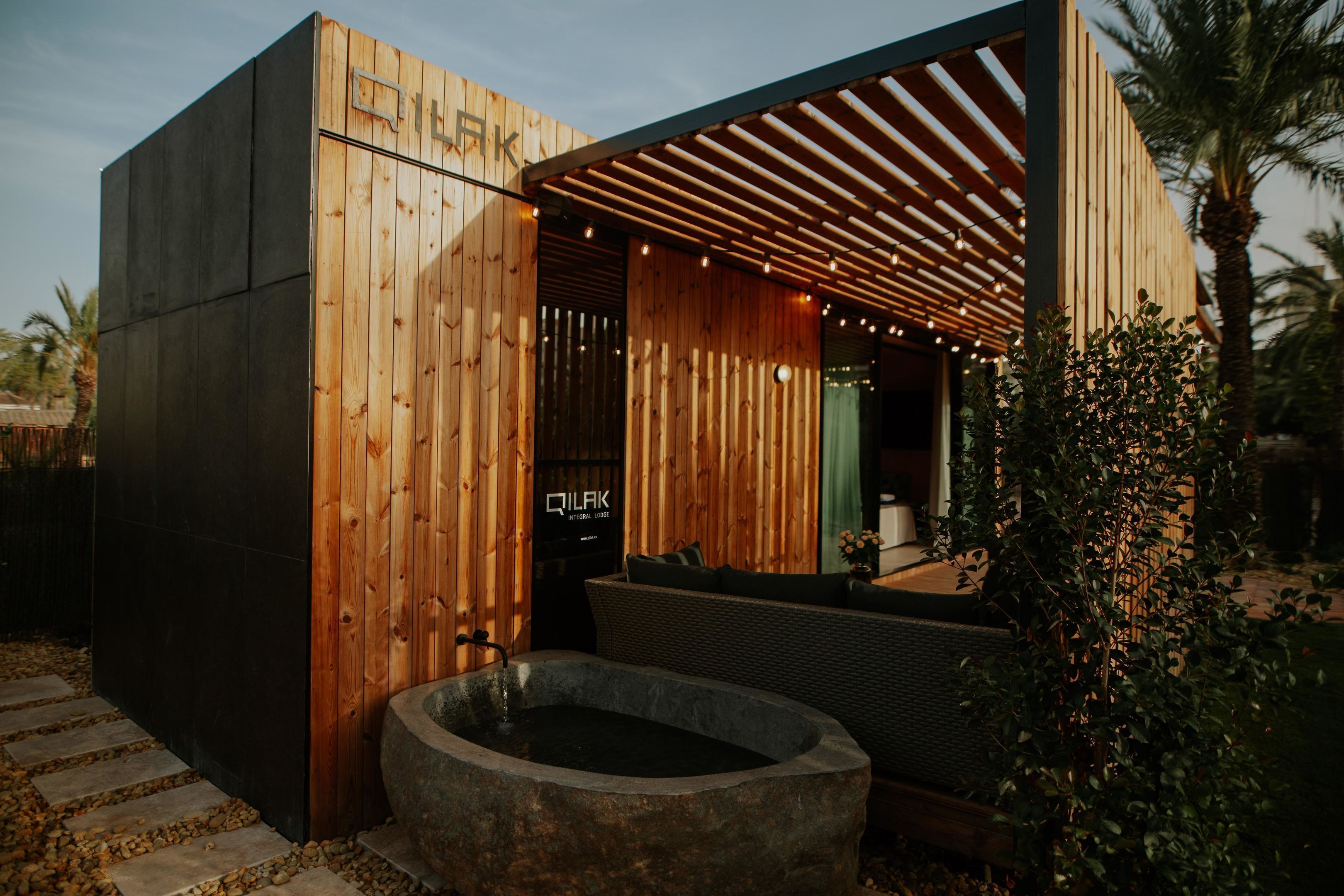 Ein modernes Gebäude mit Holzfassade, einem Steinelement als Wasserspiel und einer Sitzgelegenheit.