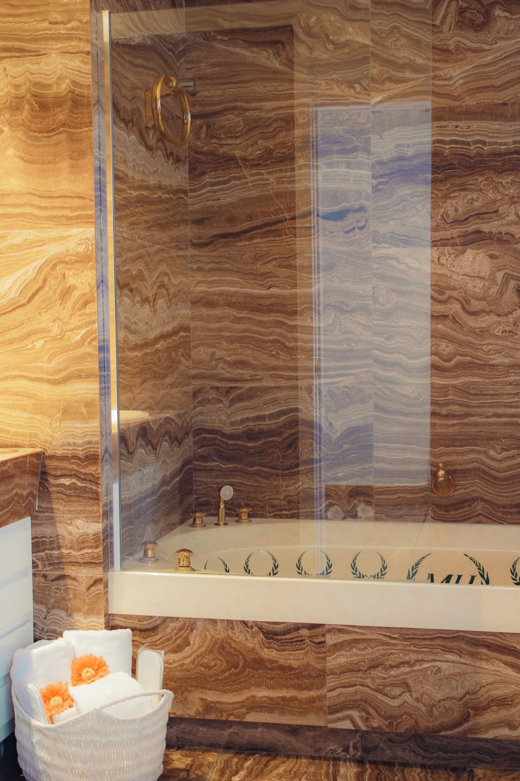 A bathroom with a marble wall, a glass shower enclosure, and a white bathtub.