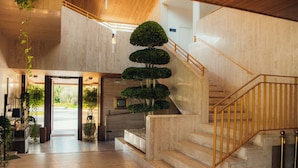 Un interior moderno con una escalera, un árbol grande en maceta y vistas al exterior.