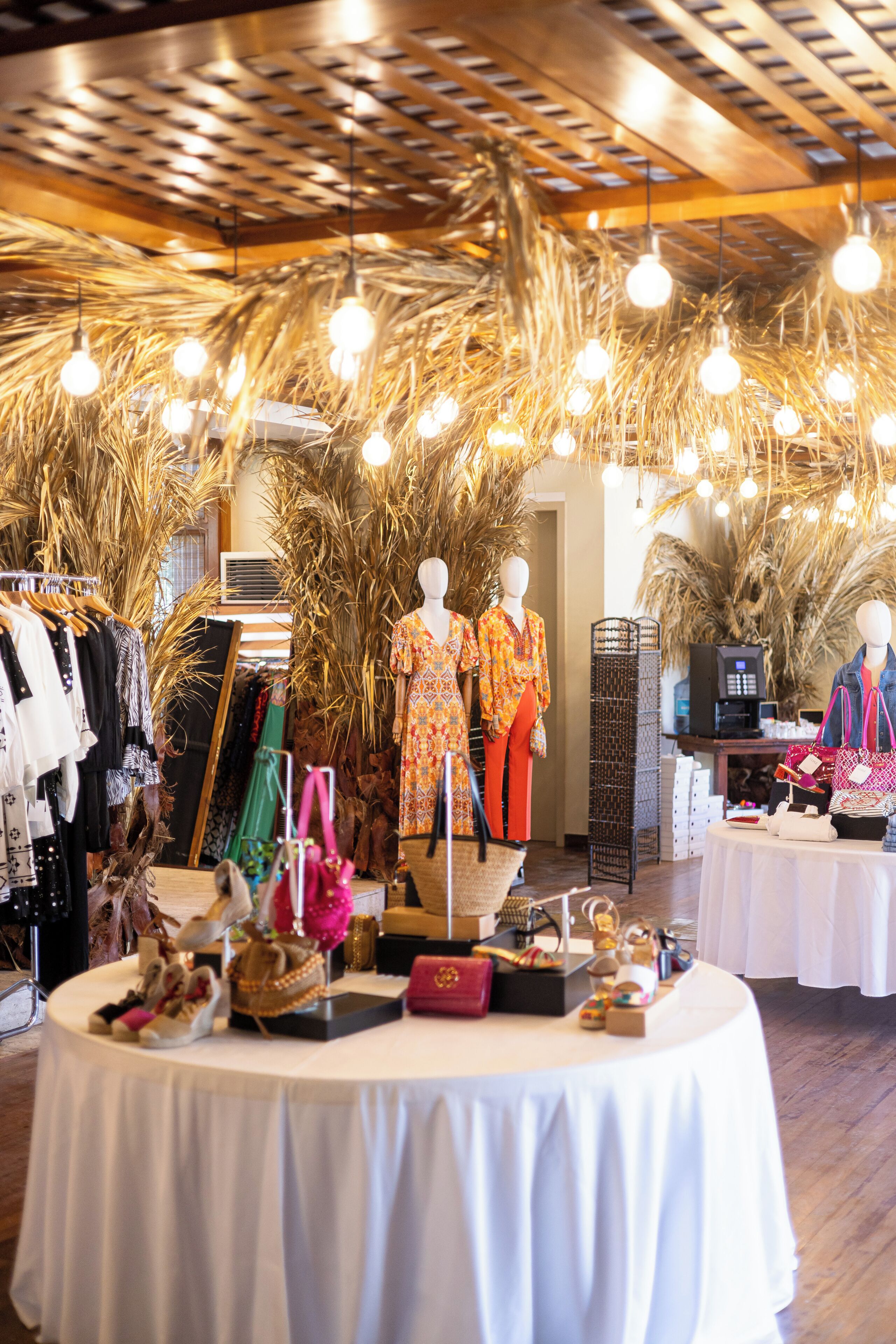L’intérieur d’un hôtel-boutique présente une table ronde centrale où sont exposés divers objets, entourée de présentoirs à vêtements et de mannequins.
