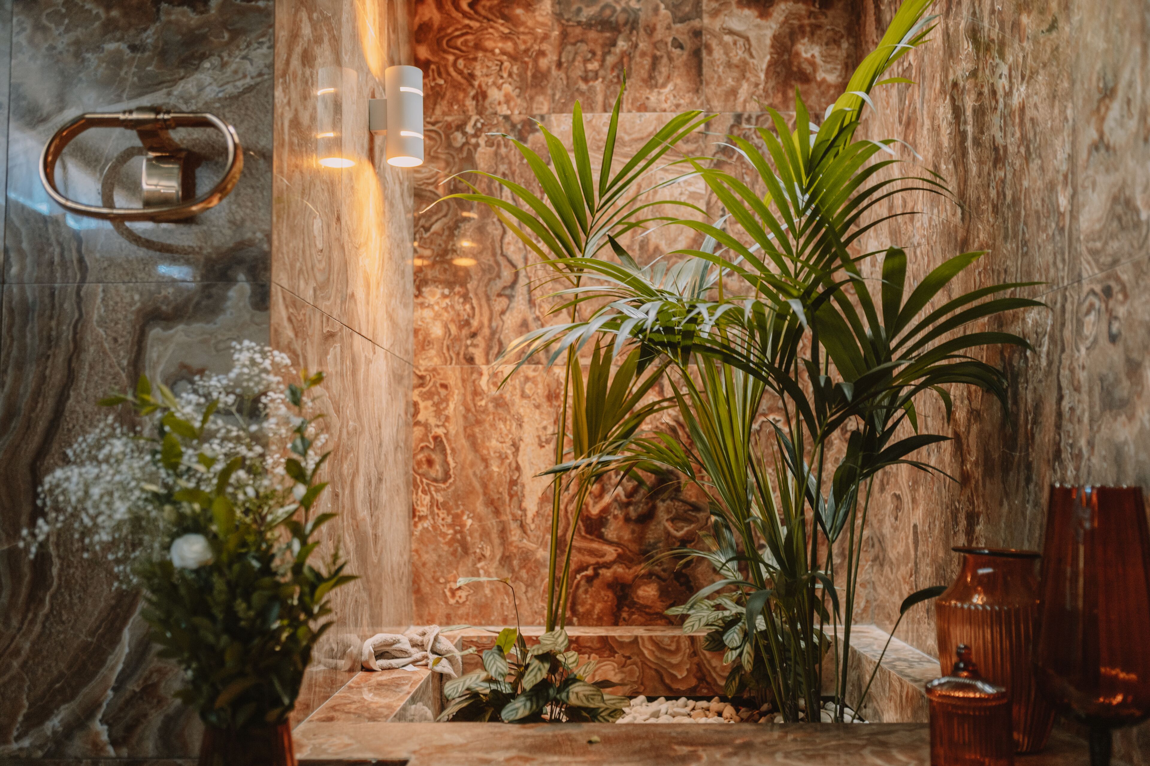 Una habitación con pared de mármol, un banco de madera y plantas en macetas.