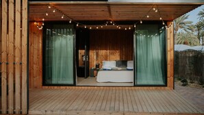 Una terraza de madera con una cama y cortinas, una mesita pequeña y una mesita de noche.