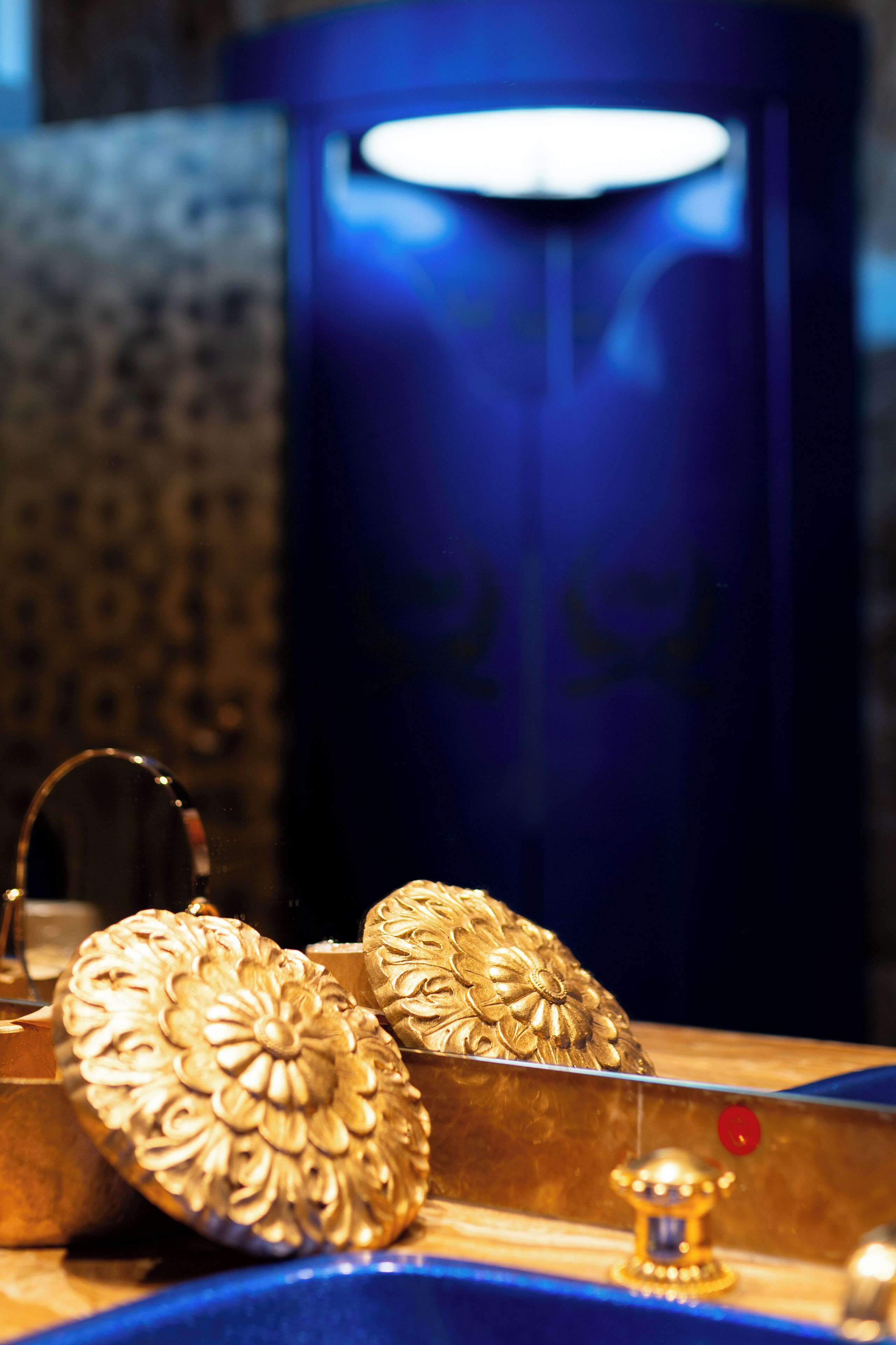 A close-up of ornate golden objects, possibly jewelry, displayed on a reflective surface with a blue background.
