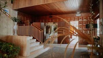 Un interior de madera con una escalera, un mostrador de recepción y un letrero que dice "SALIDA".