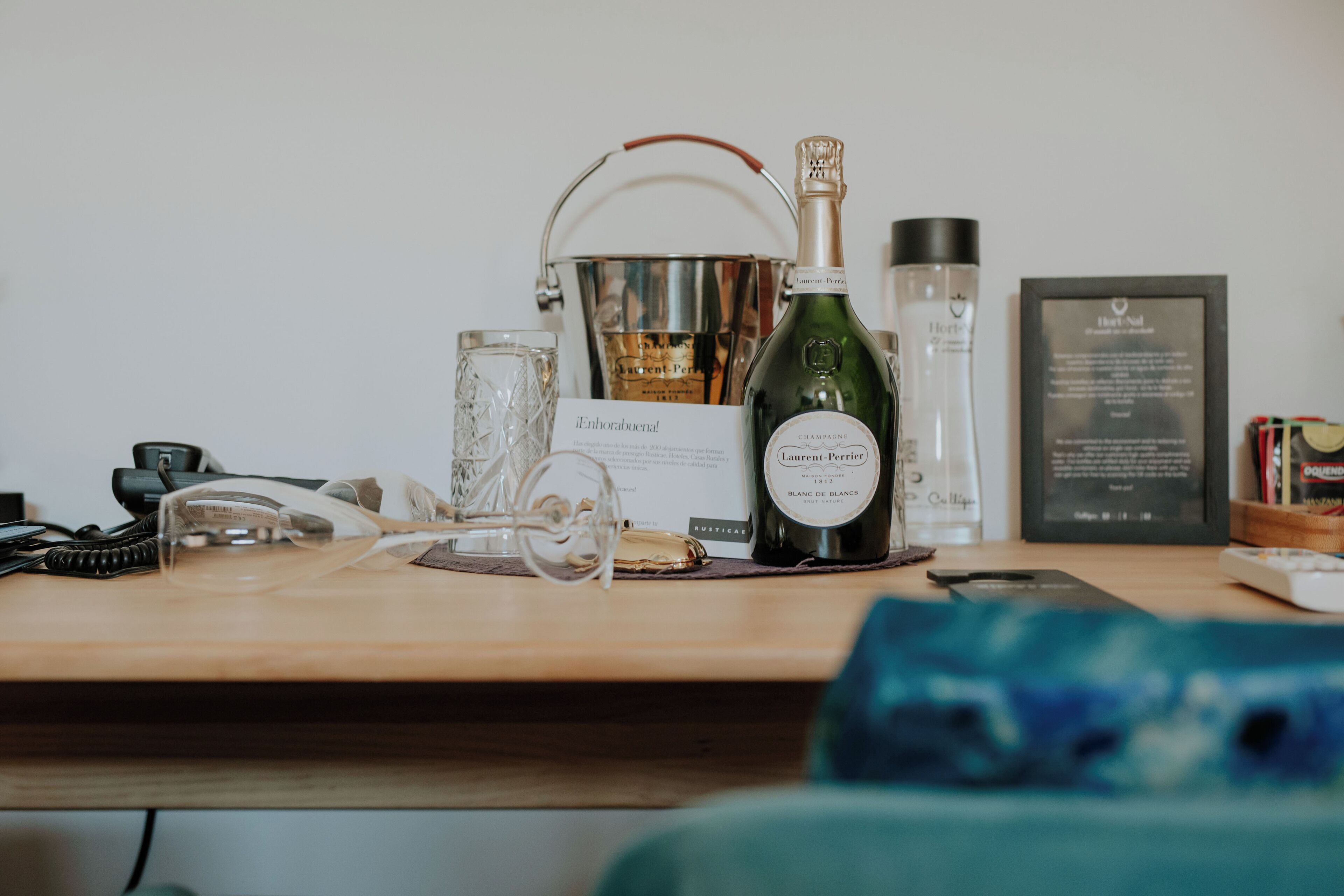 Een houten bureau met een champagnefles, een glas, een fles lotion, een ingelijst certificaat en een telefoon.