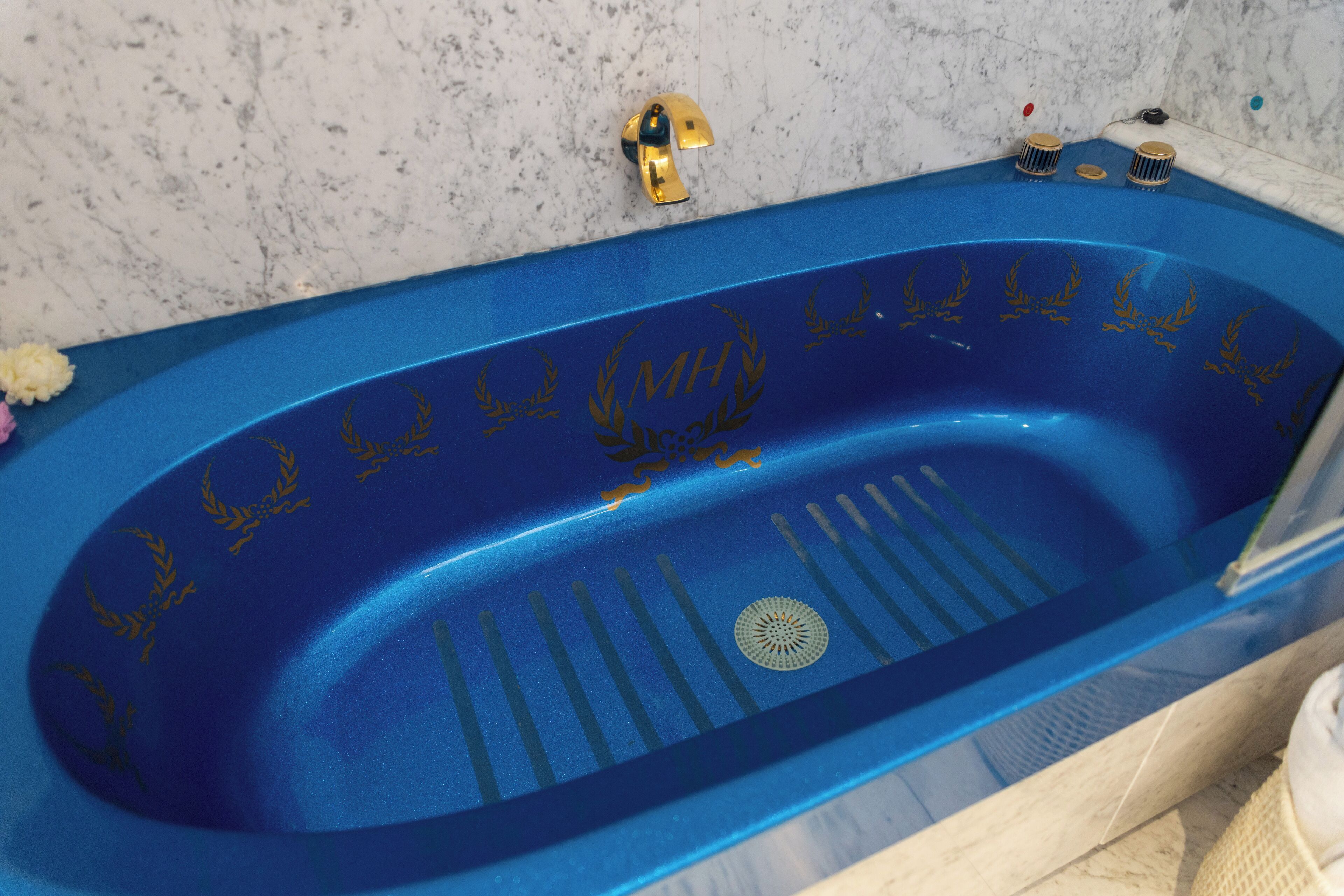 A blue bathtub with gold laurel wreaths and a drain.