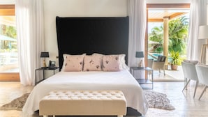 Un dormitorio amplio con una cama grande, un banco tapizado y vistas al área de la piscina exterior.