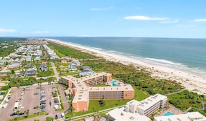 Vista aérea de un hotel costero con varias construcciones, un estacionamiento y una playa.