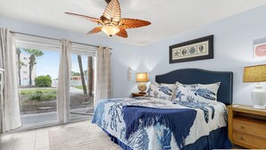 Een slaapkamer met een bed, een plafondventilator, een nachtkastje, een lamp en uitzicht op het omliggende landschap.