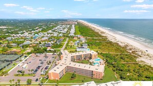 Luchtbeeld van een hotel aan de kust, met een ligging direct aan het strand, een parkeerplaats en een zwembad.