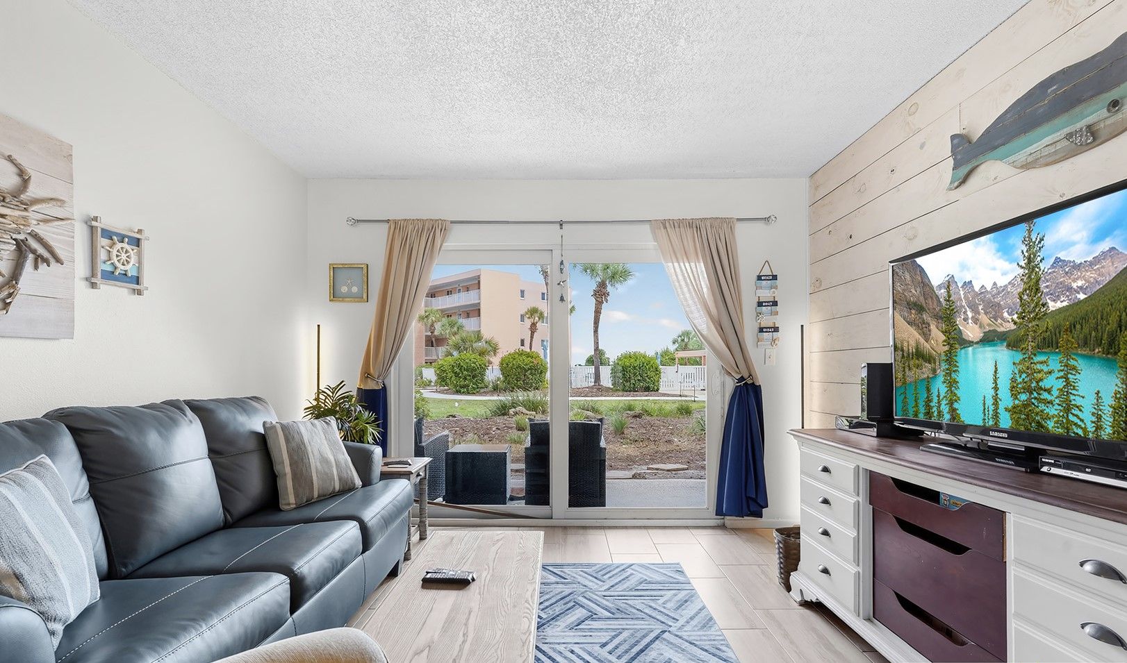 Un salon moderne avec un canapé en cuir, un téléviseur à écran plat et une porte-fenêtre coulissante donnant sur un balcon.