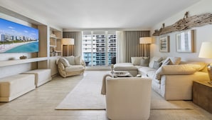 A modern living room with a large flat-screen TV, comfortable seating, and a view of a cityscape through large windows. - Luxurious 3/3 Ocean View Condo 1107 - Located at 1 Hotel & Homes South Beach (Miami Beach)