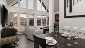 A dining area with a table set for two, large windows, a sofa, and a television on a stand. - PRIME SKI-IN/OUT LOCATION - Park City Mountain Resort Village & Base (Park City)