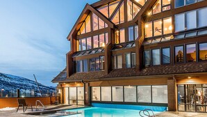 A large, multi-story building with a swimming pool, large windows, and a ski slope in the background. - PRIME SKI-IN/OUT LOCATION - Park City Mountain Resort Village & Base (Park City)