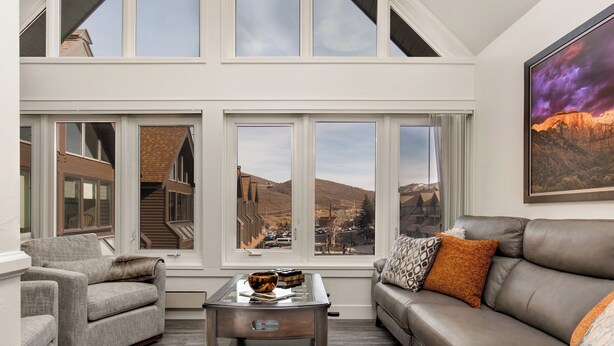 A modern living room with a sofa, armchair, and coffee table. Large windows offer views of a mountainous landscape. - PRIME SKI-IN/OUT LOCATION - Park City Mountain Resort Village & Base (Park City)