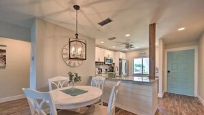A modern kitchen with white cabinetry, a central island, and a dining area with white chairs and a chandelier.