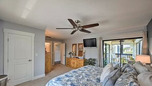 A bedroom with a bed, ceiling fan, dresser, TV, and sliding glass doors leading to an outdoor area.